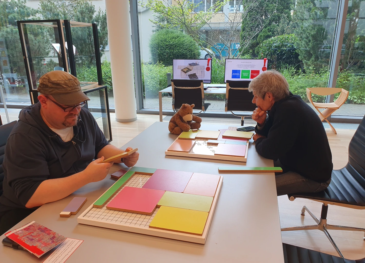 Jens, der Bär und Ulrike knobeln an einem Puzzlespiel.